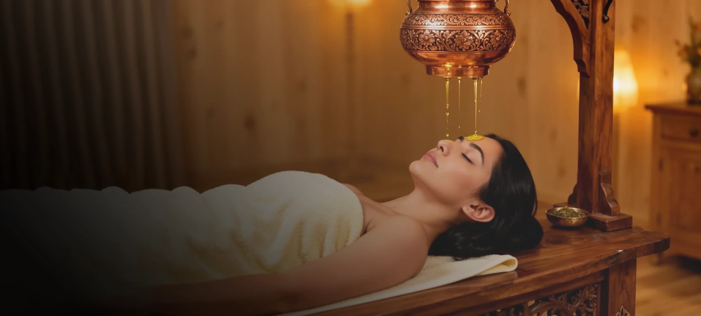 Woman receiving Shirodhara — a warm herbal oil stream over the forehead — in an Ayurvedic treatment room